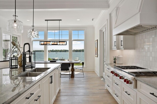 kitchen featuring light wood-type flooring, white cabinetry, custom range hood, light stone countertops, and a water view