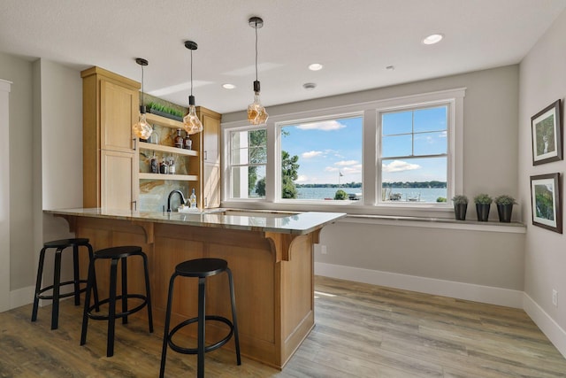 bar with light wood-type flooring, light stone countertops, decorative light fixtures, and a water view