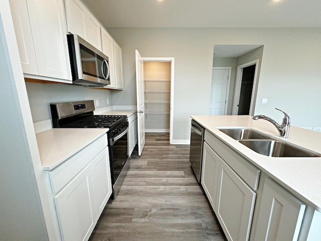 kitchen with appliances with stainless steel finishes, light hardwood / wood-style flooring, white cabinetry, and sink