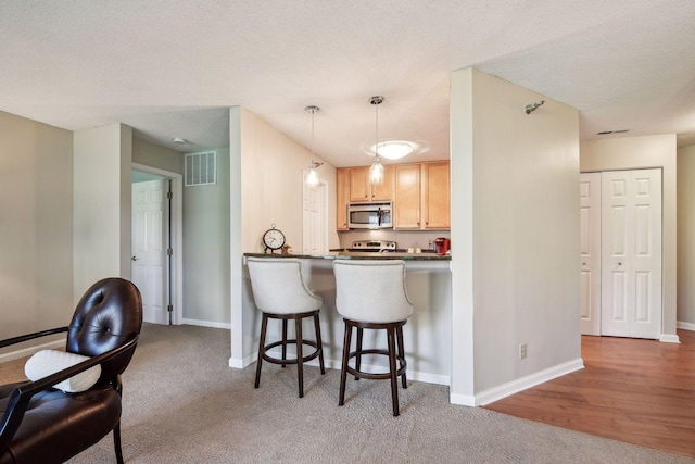 kitchen featuring pendant lighting, a kitchen bar, kitchen peninsula, stainless steel appliances, and light brown cabinets