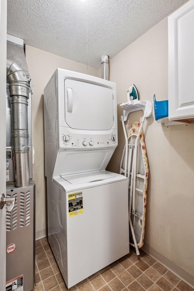 laundry room with stacked washer and dryer, a textured ceiling, and cabinets