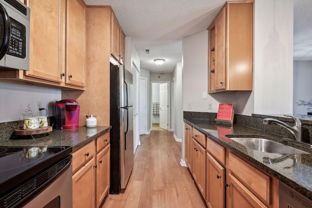 kitchen featuring sink, dark stone counters, stainless steel appliances, a textured ceiling, and light hardwood / wood-style flooring