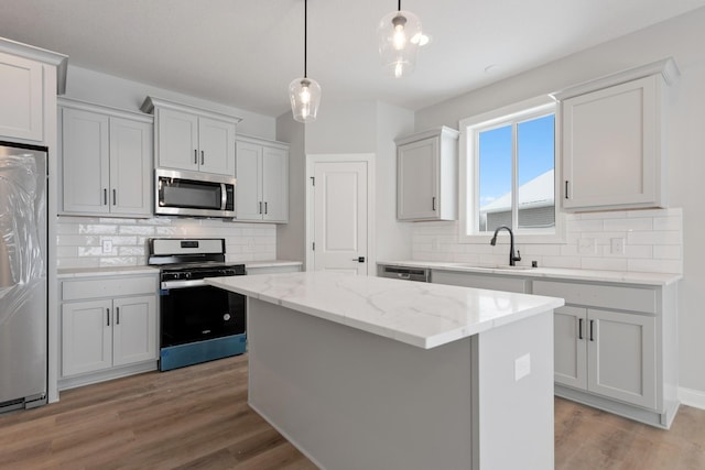 kitchen featuring light stone countertops, a kitchen island, stainless steel appliances, sink, and hanging light fixtures