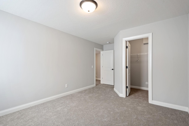 unfurnished bedroom featuring light colored carpet, a closet, a spacious closet, and a textured ceiling