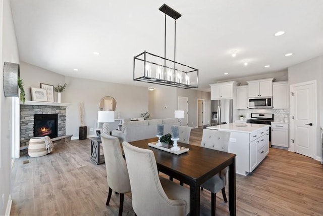 dining space featuring light wood-style floors, recessed lighting, a stone fireplace, and baseboards