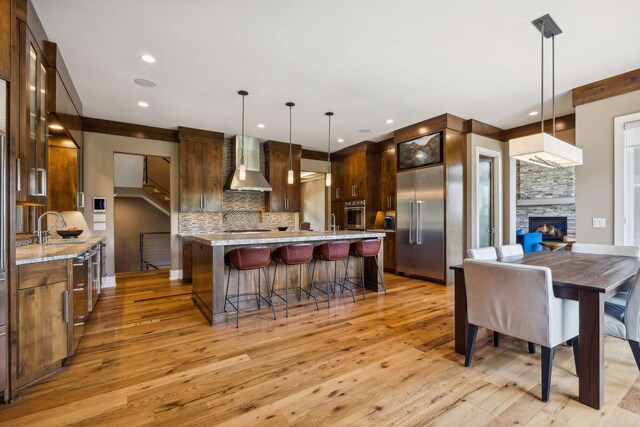 kitchen with tasteful backsplash, light wood-type flooring, pendant lighting, wall chimney exhaust hood, and a fireplace