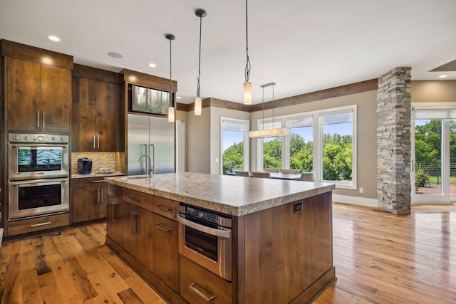 kitchen featuring appliances with stainless steel finishes, a kitchen island with sink, light hardwood / wood-style floors, and decorative light fixtures