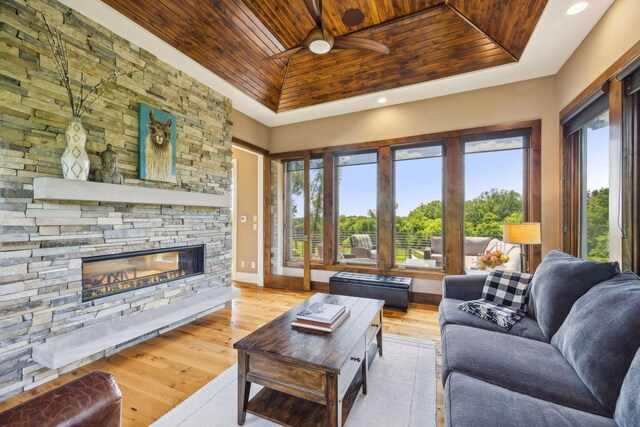 living room with wood ceiling, a stone fireplace, light wood-type flooring, and a tray ceiling