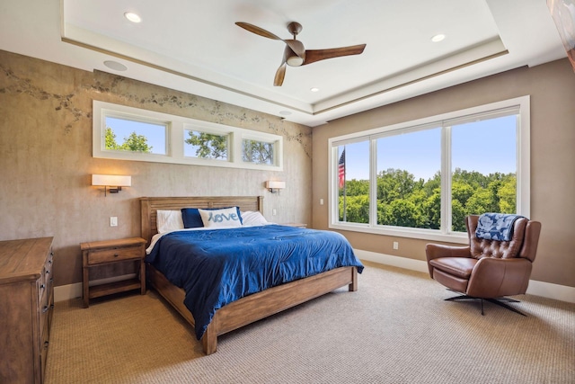 bedroom with ceiling fan, light colored carpet, and a tray ceiling