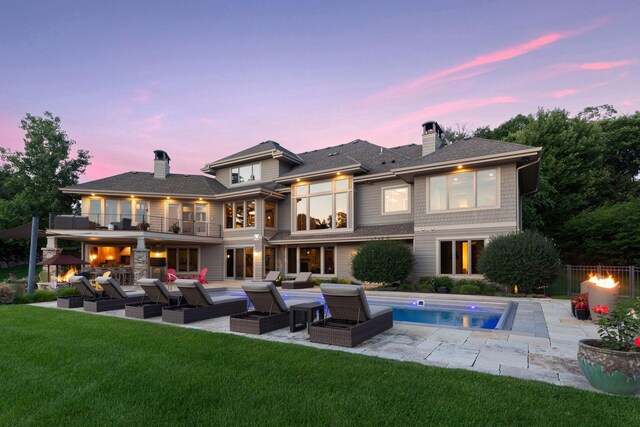 back house at dusk featuring an outdoor hangout area, a balcony, a patio area, and a yard