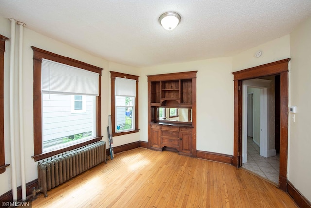 unfurnished room featuring a textured ceiling, light hardwood / wood-style floors, and radiator heating unit