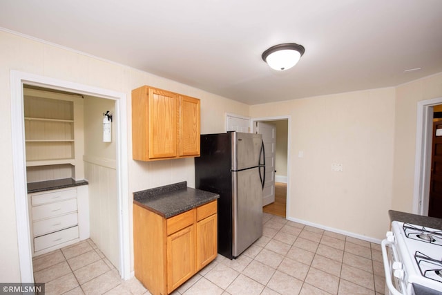 kitchen featuring light tile patterned flooring, white range with gas stovetop, and stainless steel refrigerator