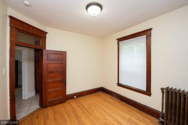 unfurnished room featuring radiator, a textured ceiling, and light wood-type flooring