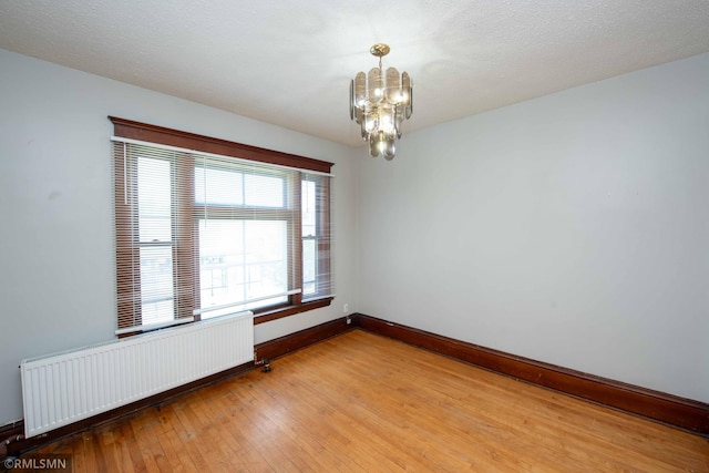 empty room with an inviting chandelier, radiator, hardwood / wood-style flooring, and a textured ceiling