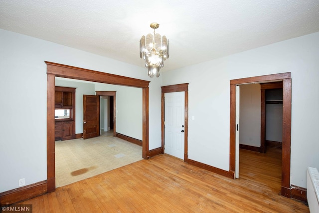 spare room featuring light wood-type flooring, a textured ceiling, radiator heating unit, and a chandelier