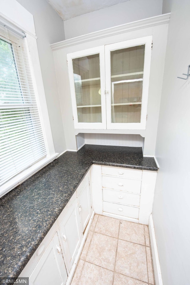 kitchen featuring dark stone counters, white cabinets, and light tile patterned flooring