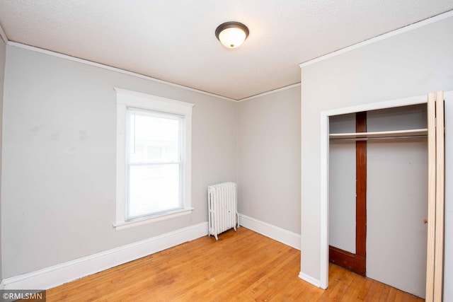 unfurnished bedroom with radiator heating unit, a closet, a textured ceiling, crown molding, and hardwood / wood-style flooring