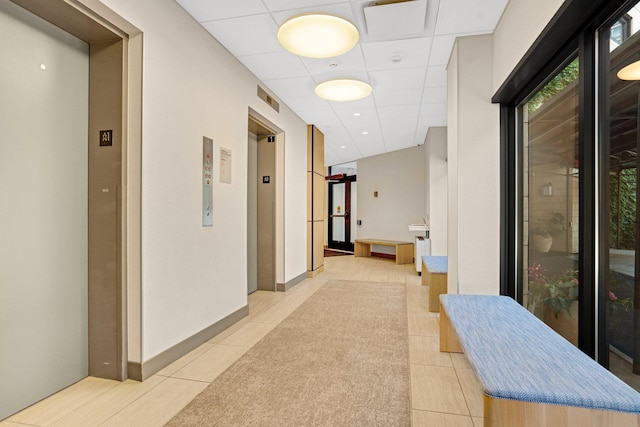 hallway with light tile patterned floors, elevator, and a drop ceiling