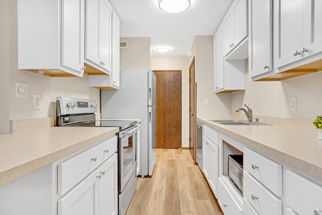 kitchen featuring light countertops, a sink, light wood-style floors, stainless steel appliances, and white cabinets