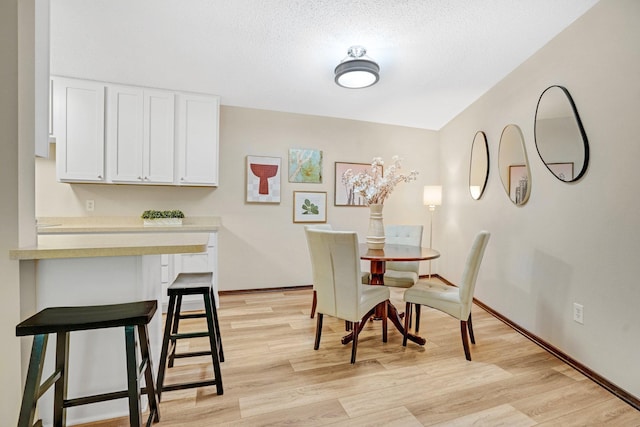 dining area featuring baseboards, light wood-type flooring, and a textured ceiling