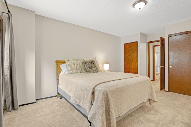 bedroom with multiple closets, light carpet, and a textured ceiling