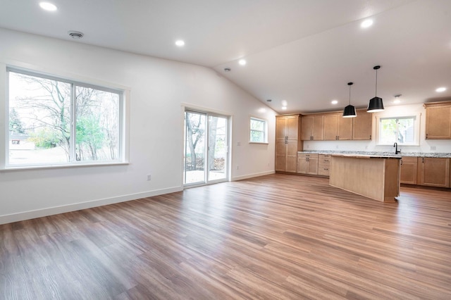 kitchen featuring light stone countertops, light wood-type flooring, a center island, hanging light fixtures, and vaulted ceiling