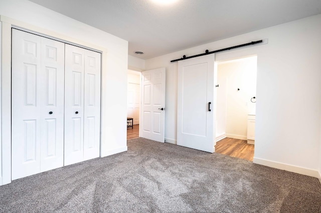 unfurnished bedroom featuring a barn door, carpet floors, and a closet