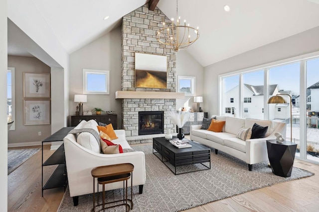 living room with an inviting chandelier, high vaulted ceiling, wood-type flooring, and a stone fireplace