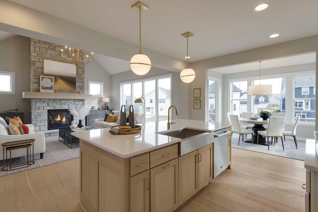 kitchen featuring light hardwood / wood-style flooring, dishwasher, pendant lighting, a stone fireplace, and sink