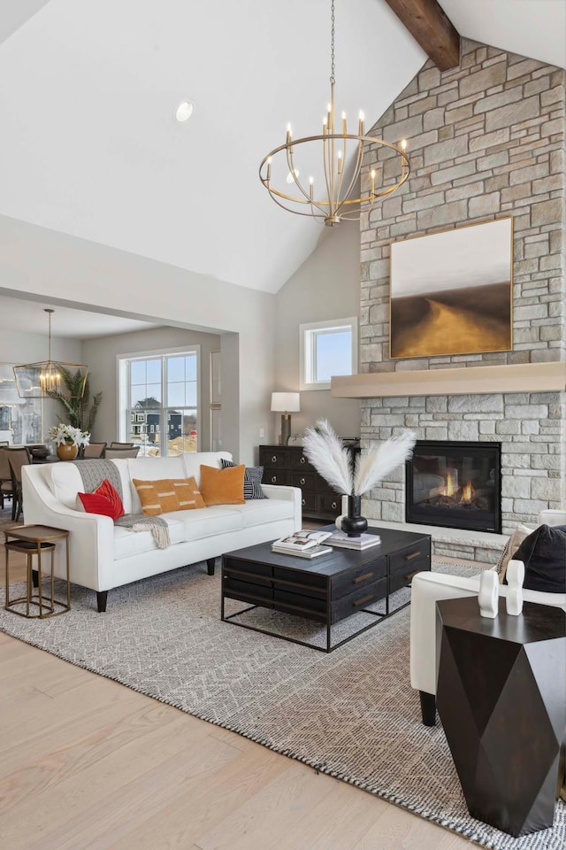 living room featuring beamed ceiling, hardwood / wood-style floors, a stone fireplace, high vaulted ceiling, and a chandelier