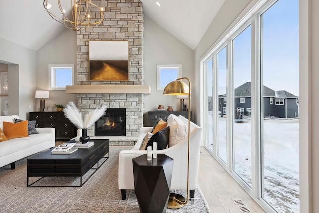 living room featuring hardwood / wood-style flooring, a stone fireplace, high vaulted ceiling, and a chandelier