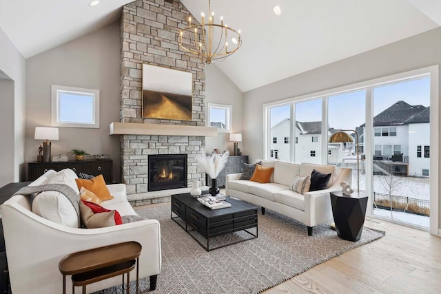 living room with high vaulted ceiling, a fireplace, light hardwood / wood-style flooring, and a notable chandelier