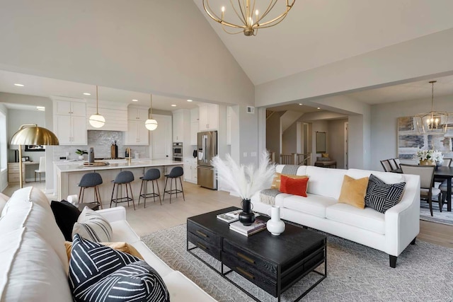 living room featuring a notable chandelier, high vaulted ceiling, and light wood-type flooring