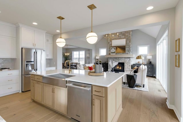 kitchen with a stone fireplace, appliances with stainless steel finishes, light hardwood / wood-style flooring, and a kitchen island with sink