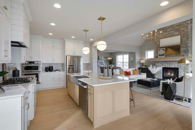 kitchen featuring light hardwood / wood-style flooring, appliances with stainless steel finishes, decorative backsplash, a stone fireplace, and a center island with sink