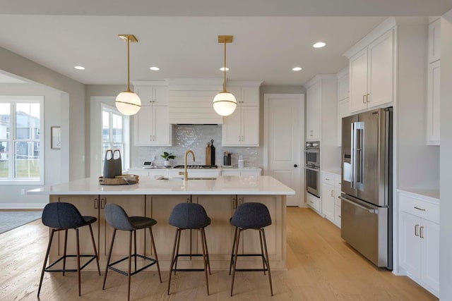 kitchen featuring white cabinetry, stainless steel appliances, pendant lighting, light hardwood / wood-style flooring, and backsplash