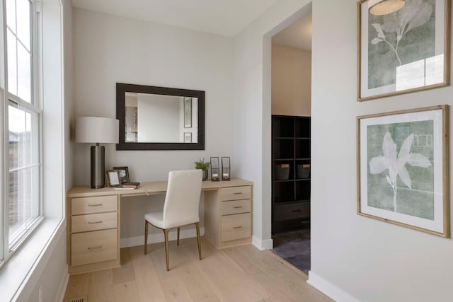 office space with a wealth of natural light, built in desk, and light hardwood / wood-style floors