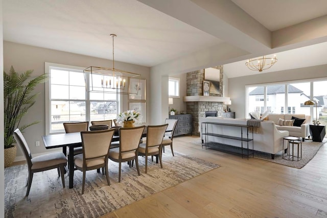 dining space featuring an inviting chandelier, wood-type flooring, and a stone fireplace