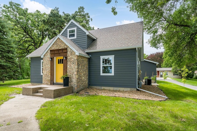 view of front facade with central AC unit, stone siding, roof with shingles, and a front yard