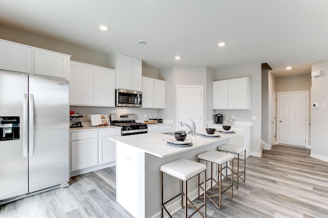 kitchen with a center island with sink, sink, appliances with stainless steel finishes, white cabinetry, and a breakfast bar area