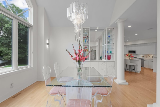 dining area with light wood-type flooring, ornate columns, an inviting chandelier, and sink