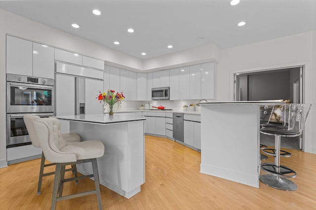 kitchen with a kitchen island, white cabinetry, light wood-type flooring, a kitchen breakfast bar, and stainless steel appliances