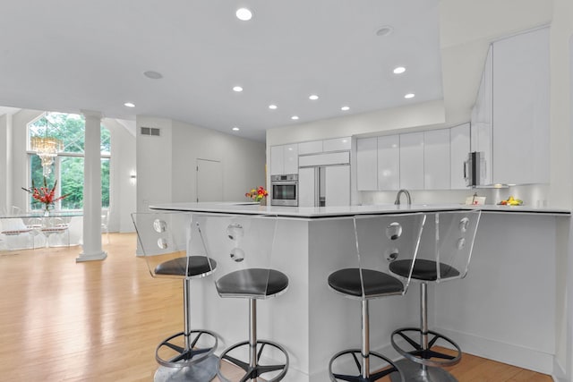 kitchen featuring a kitchen bar, white cabinets, stainless steel appliances, and decorative columns