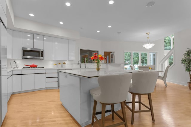 kitchen with hanging light fixtures, white cabinets, a center island, and light wood-type flooring