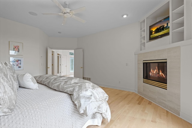 bedroom featuring ceiling fan, a tile fireplace, and hardwood / wood-style floors