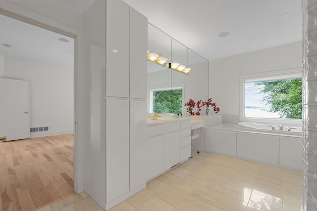 bathroom featuring a wealth of natural light, a tub to relax in, vanity, and tile patterned flooring