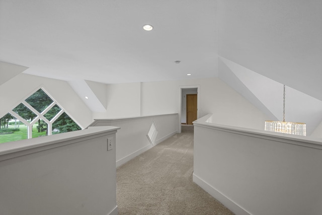 hall with light colored carpet, lofted ceiling, and a notable chandelier