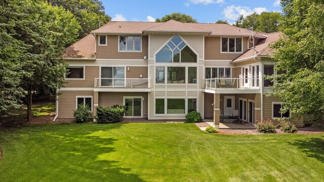 rear view of property featuring a balcony, a yard, and a patio