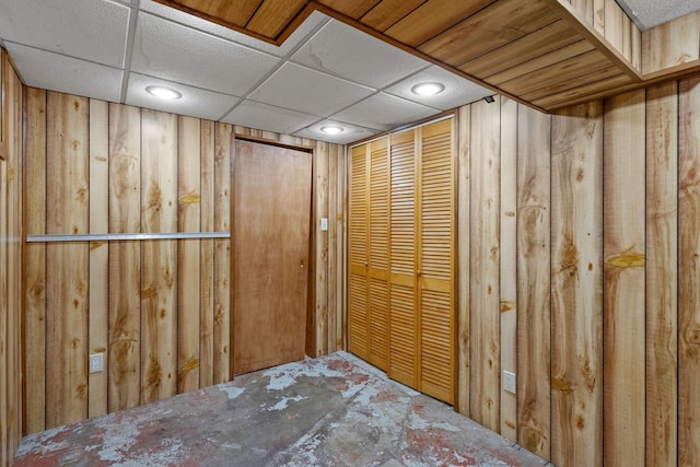 basement featuring a paneled ceiling and wood walls