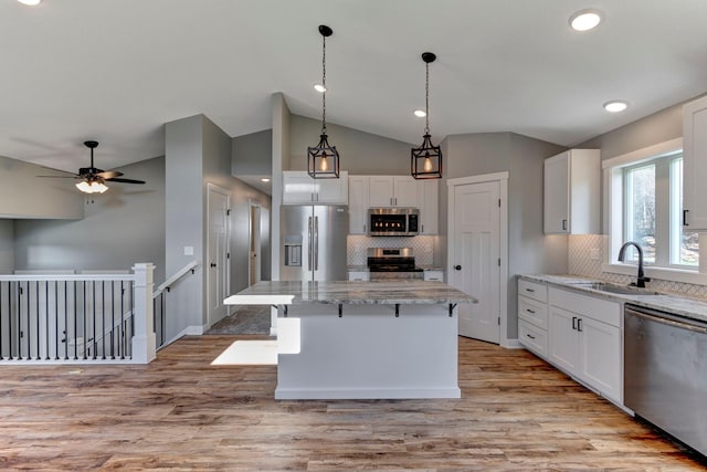 kitchen featuring white cabinetry, sink, light stone counters, appliances with stainless steel finishes, and a kitchen island